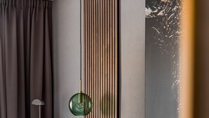 A modern bedroom with a bed, pillows, a green accent pillow, a floor lamp, and a painting on the wall.