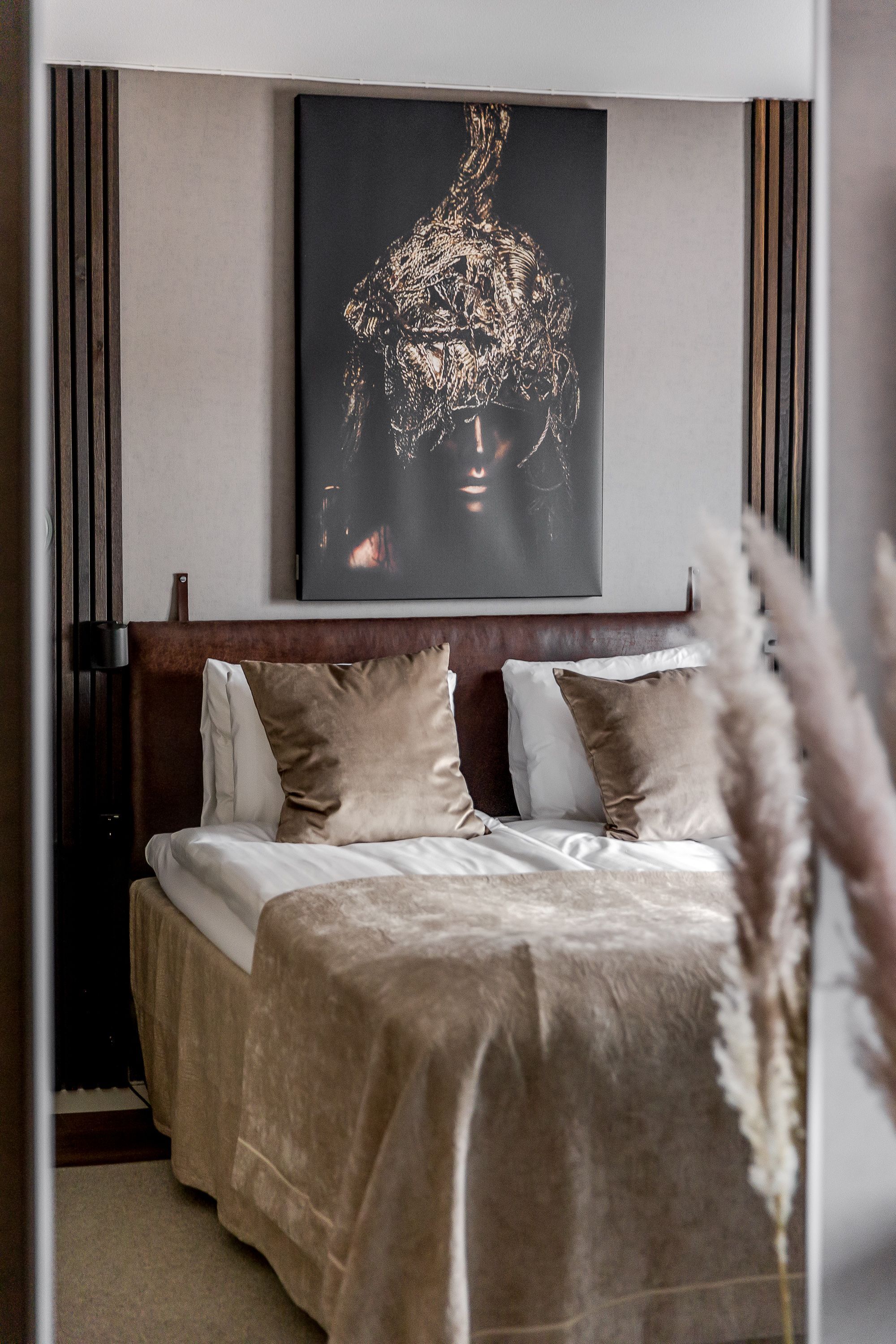A bedroom with a large bed, a headboard, and a wall-mounted artwork.