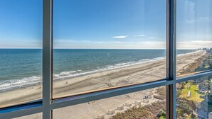 Udsigt til stranden fra et vindue, klart himmel og rolig sø.
