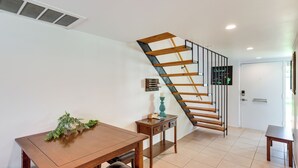 Un coin repas avec une table et des chaises en bois, une petite table d’appoint avec une bougie, et un escalier avec des marches en bois et des rampes en métal.