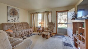 A living room with a large sofa, a chair, a television, and a bookshelf. - Family-friendly Home w/ Fire Pit ~ 10 Mi to Akron! (Akron)