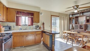 A spacious kitchen with wooden cabinets, a central island, and a dining area with wooden chairs and a table. - Family-friendly Home w/ Fire Pit ~ 10 Mi to Akron! (Akron)