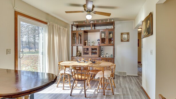A dining area with a round wooden table and chairs, a ceiling fan, and a view through a large window. - Family-friendly Home w/ Fire Pit ~ 10 Mi to Akron! (Akron)