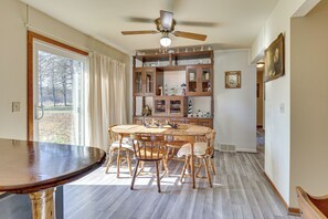 A dining area with a round wooden table and chairs, a ceiling fan, and a view through a large window. - Family-friendly Home w/ Fire Pit ~ 10 Mi to Akron! (Akron)