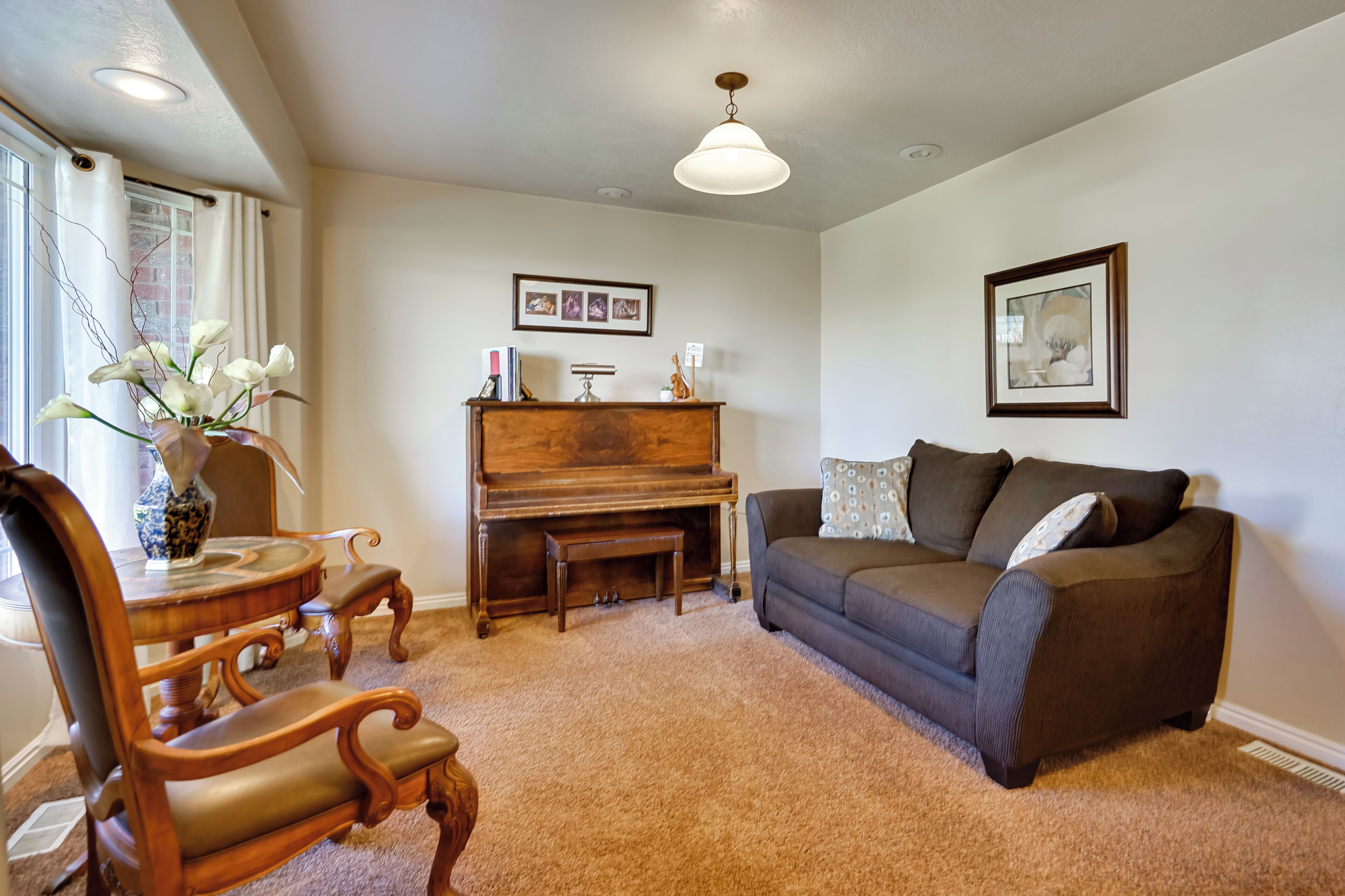 A living room with a piano, a brown sofa, a wooden coffee table, and a vase with flowers.
