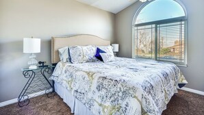 Ein Schlafzimmer mit einem Bett, zwei Nachttischen, einem Deckenventilator und einem großen Fenster mit Jalousien.