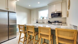 A modern kitchen with white cabinets, a stainless steel refrigerator, a built-in oven, and a large island with bar stools.