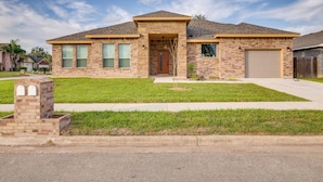 A two-story brick house with a front garage, a small front yard, and a clear sky.