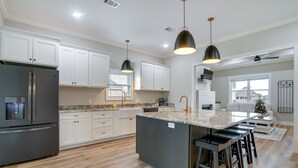 Een moderne keuken met witte kasten, een groot eiland met barkrukken, een inbouwkoelkast en hanglampen.