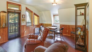 A spacious living room with a leather sofa, wooden dining table, and a fan. - Forested Coffman Cove Cabin w/ Wood-burning Stove! (Coffman Cove)