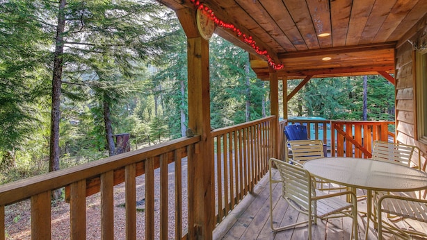 A wooden deck with a table and chairs, surrounded by a wooden railing, overlooking a forested area. - Forested Coffman Cove Cabin w/ Wood-burning Stove! (Coffman Cove)