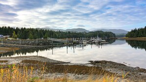 A calm lake with a dock and boats, surrounded by forested hills and a clear sky. - Forested Coffman Cove Cabin w/ Wood-burning Stove! (Coffman Cove)