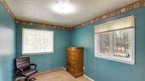 A room with teal walls, a wooden dresser, a leather office chair, and two windows with blinds.