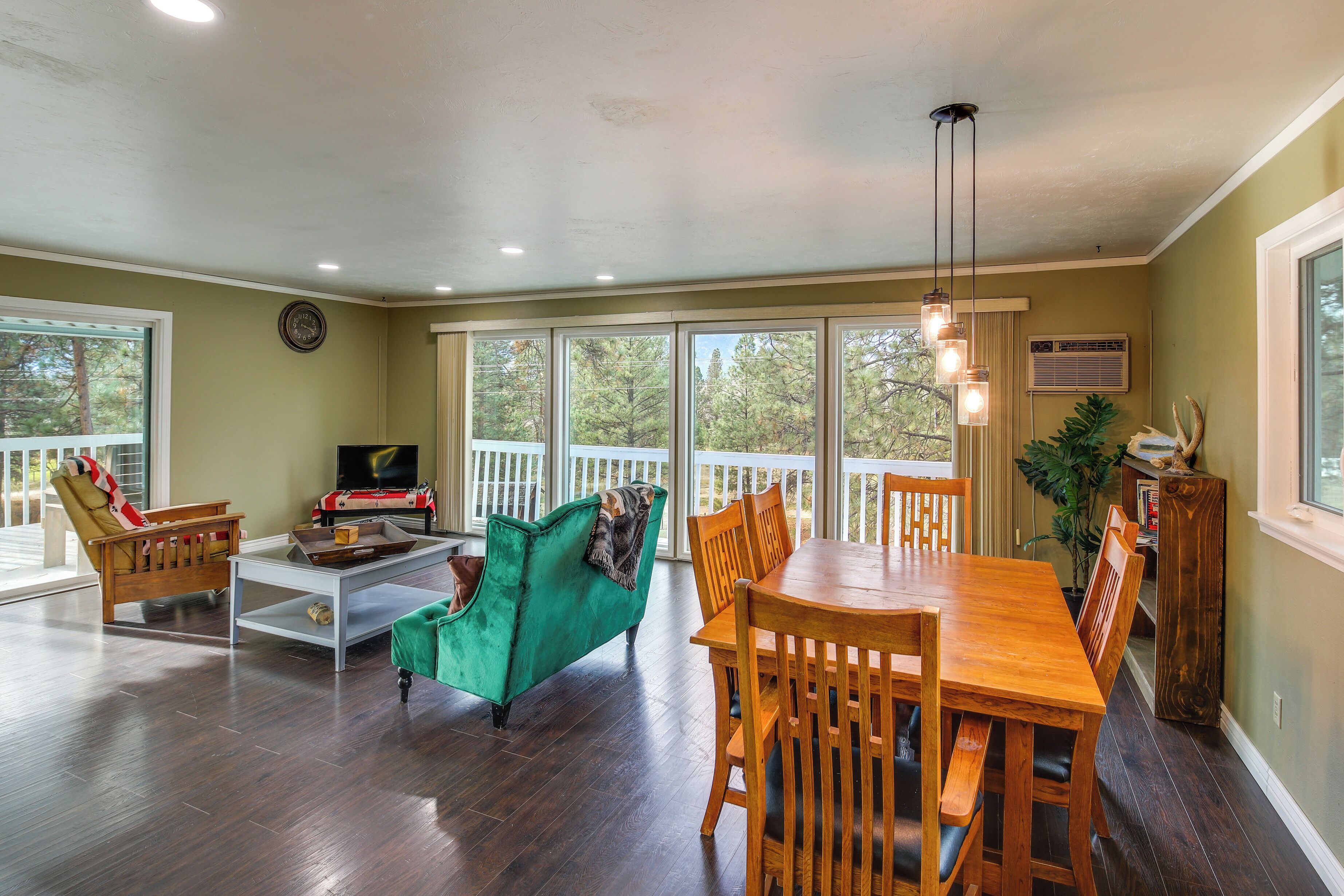 A spacious living room with a green sofa, wooden dining table, and a large window with a view of trees.