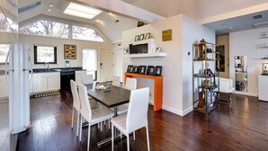 Une cuisine moderne avec des meubles blancs, une table à manger avec des chaises et une étagère intégrée pour le micro-ondes.