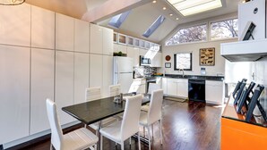Une cuisine moderne avec des meubles blancs, un plan de travail noir et un coin repas avec des chaises blanches.
