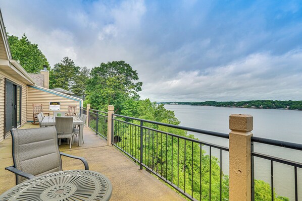 A balcony with outdoor furniture, a view of a lake, and a building with a sign. - Boat Slip & Water Views: Lake Ozark Condo (Lake Ozark)