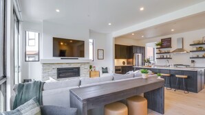 Un área de estar moderna y de concepto abierto con chimenea, un televisor grande y una cocina con taburetes de bar.