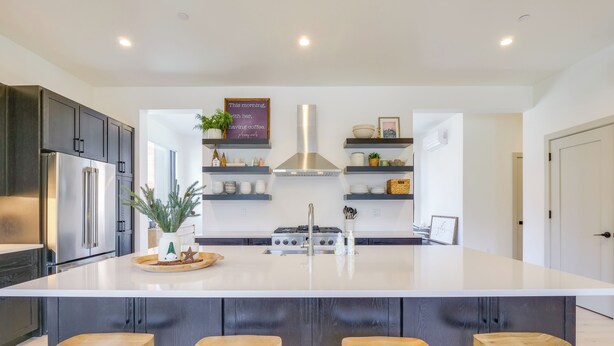 Una cocina moderna con una isla grande, armarios oscuros, electrodomésticos de acero inoxidable y taburetes de madera.