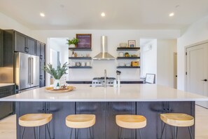 A modern kitchen with a large island, dark cabinets, stainless steel appliances, and wooden stools.