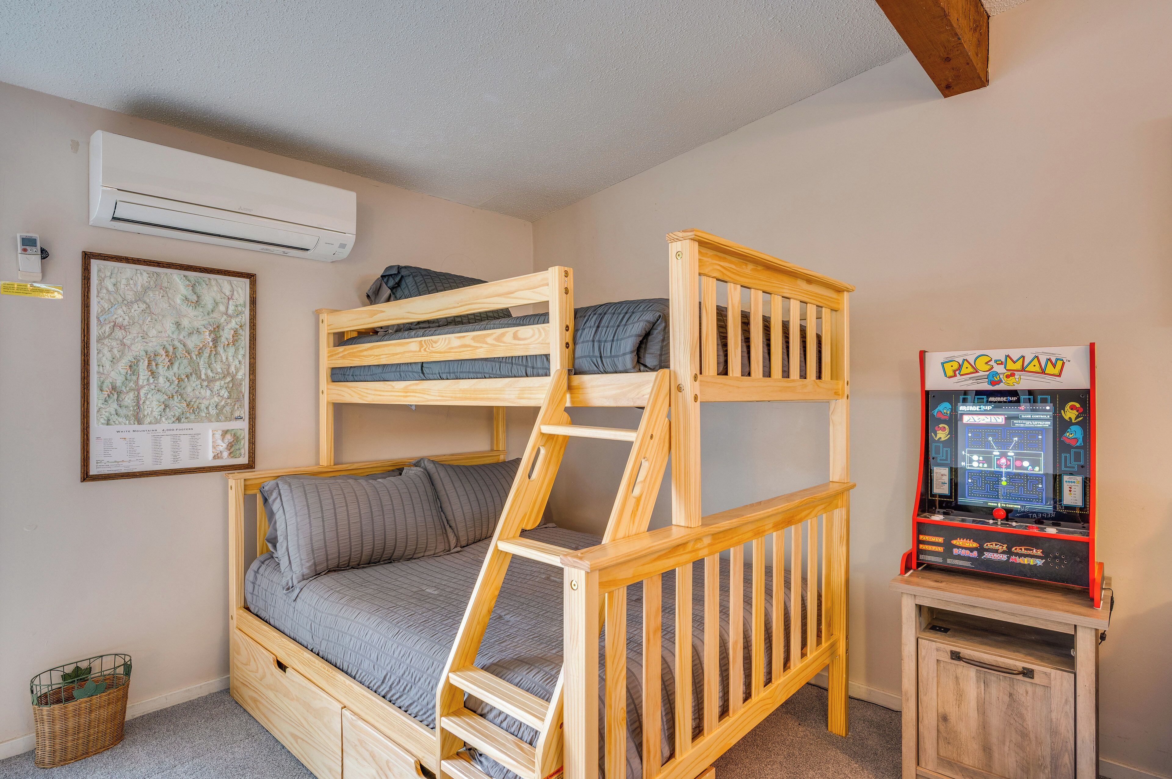 Una cama litera con escalera, un pequeño armario de madera y una máquina arcade de Pac-Man.