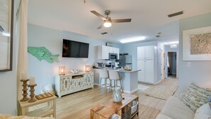 Un salón amplio con un sofá grande, una mesa de centro de madera y una zona de cocina con armarios blancos y un taburete de bar.