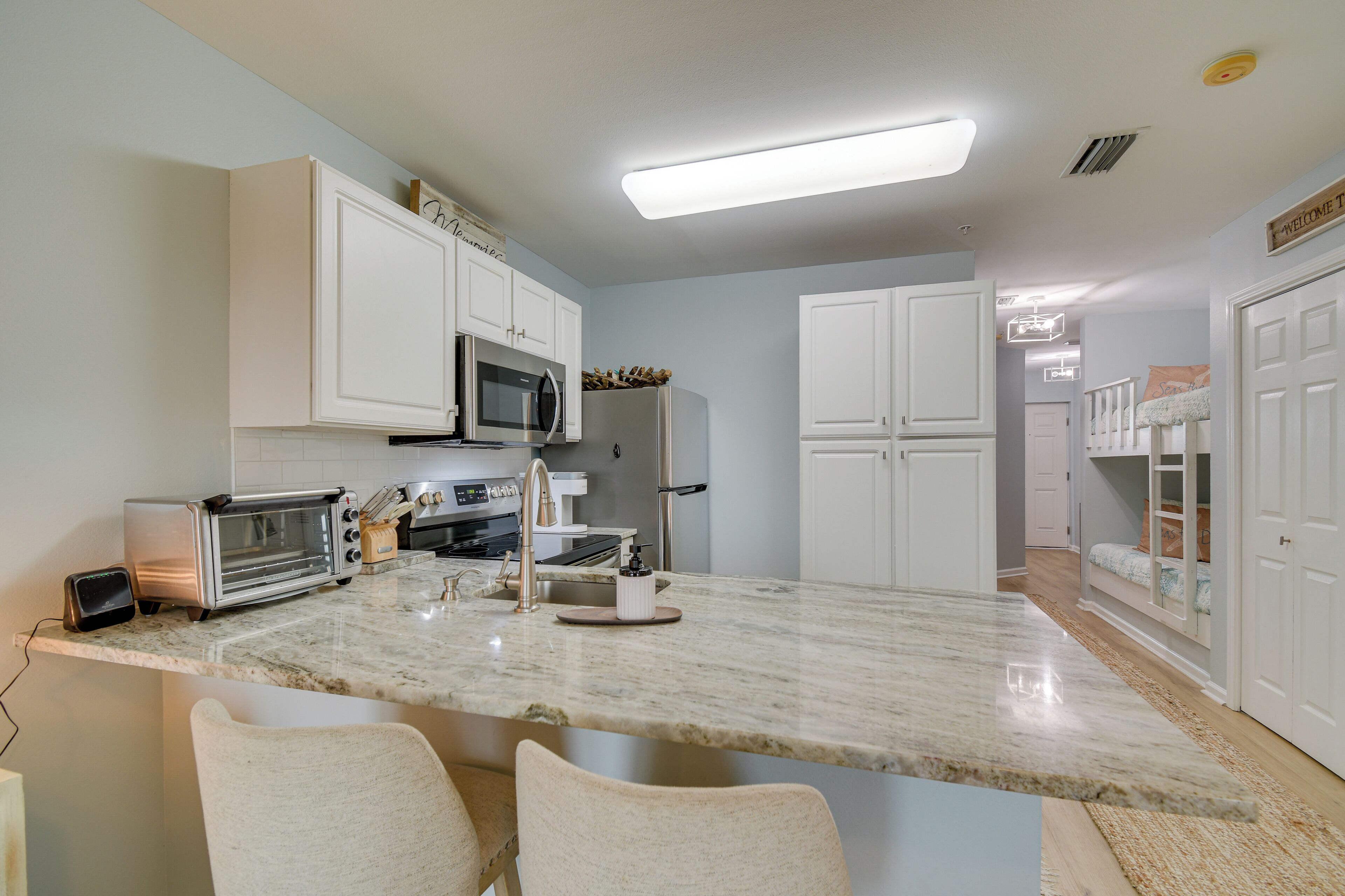 A modern kitchen with white cabinets, a built-in microwave, a refrigerator, and a granite countertop.