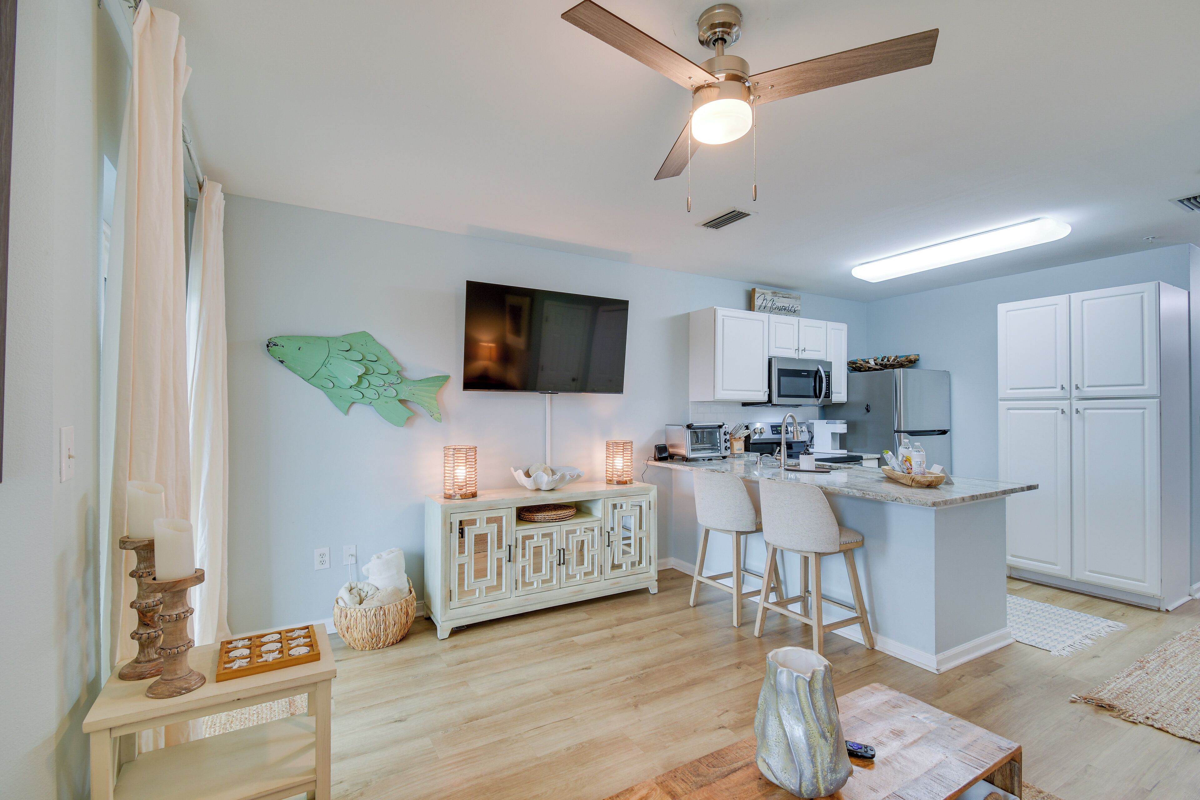 A modern kitchen with white cabinets, a microwave, and a large flat-screen TV.