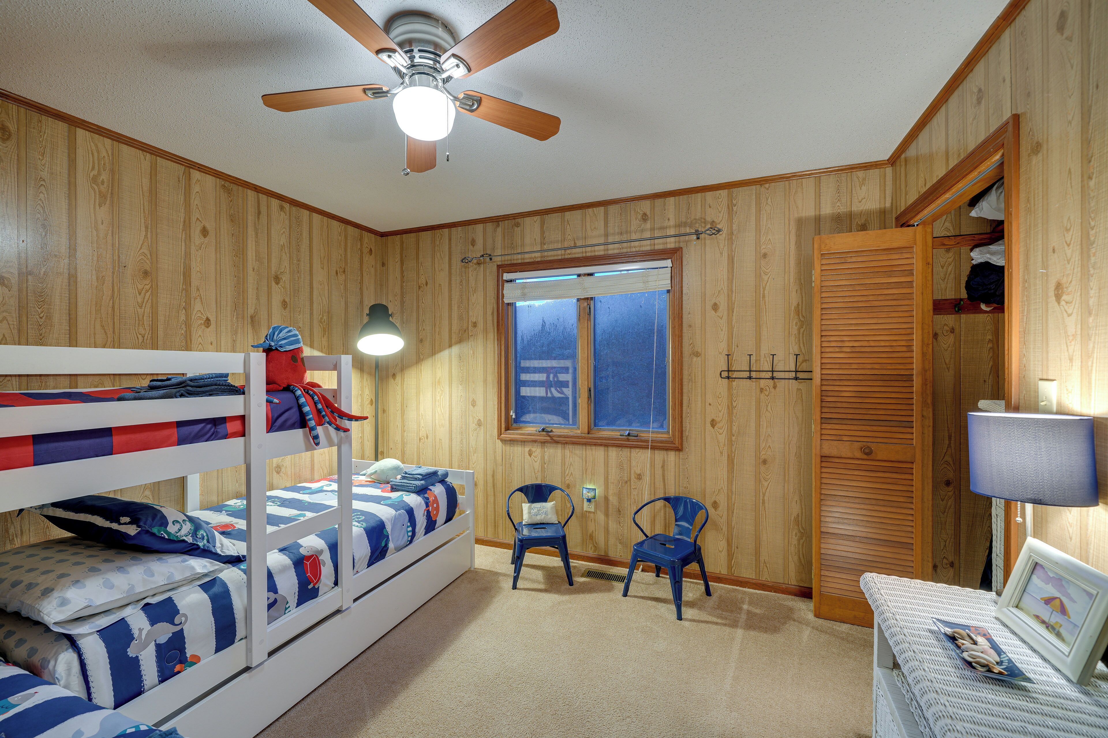 Een slaapkamer met stapelbed, plafondventilator, twee stoelen, een raam en een deur.