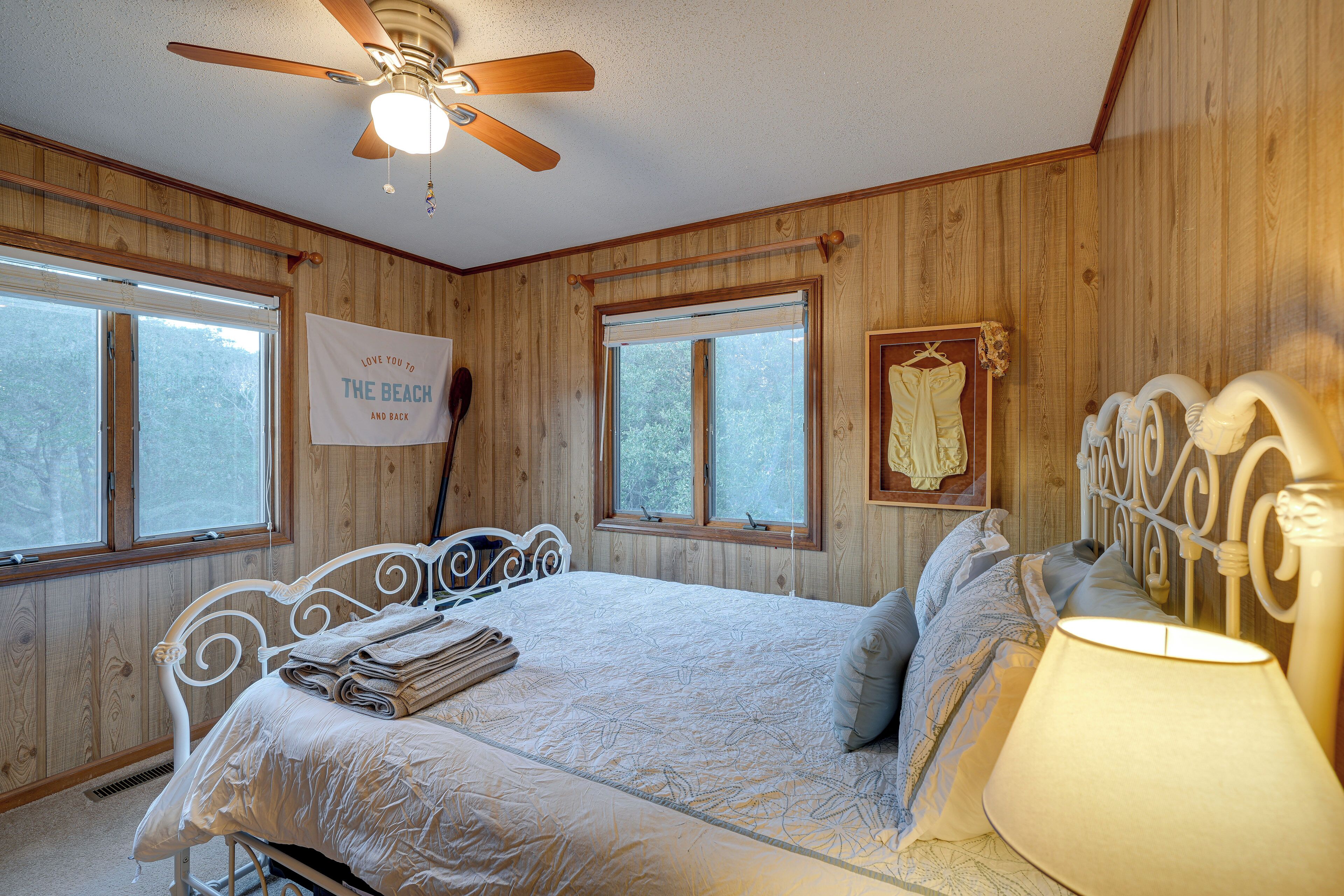 A bedroom with a bed, a ceiling fan, two windows, and a sign on the wall.