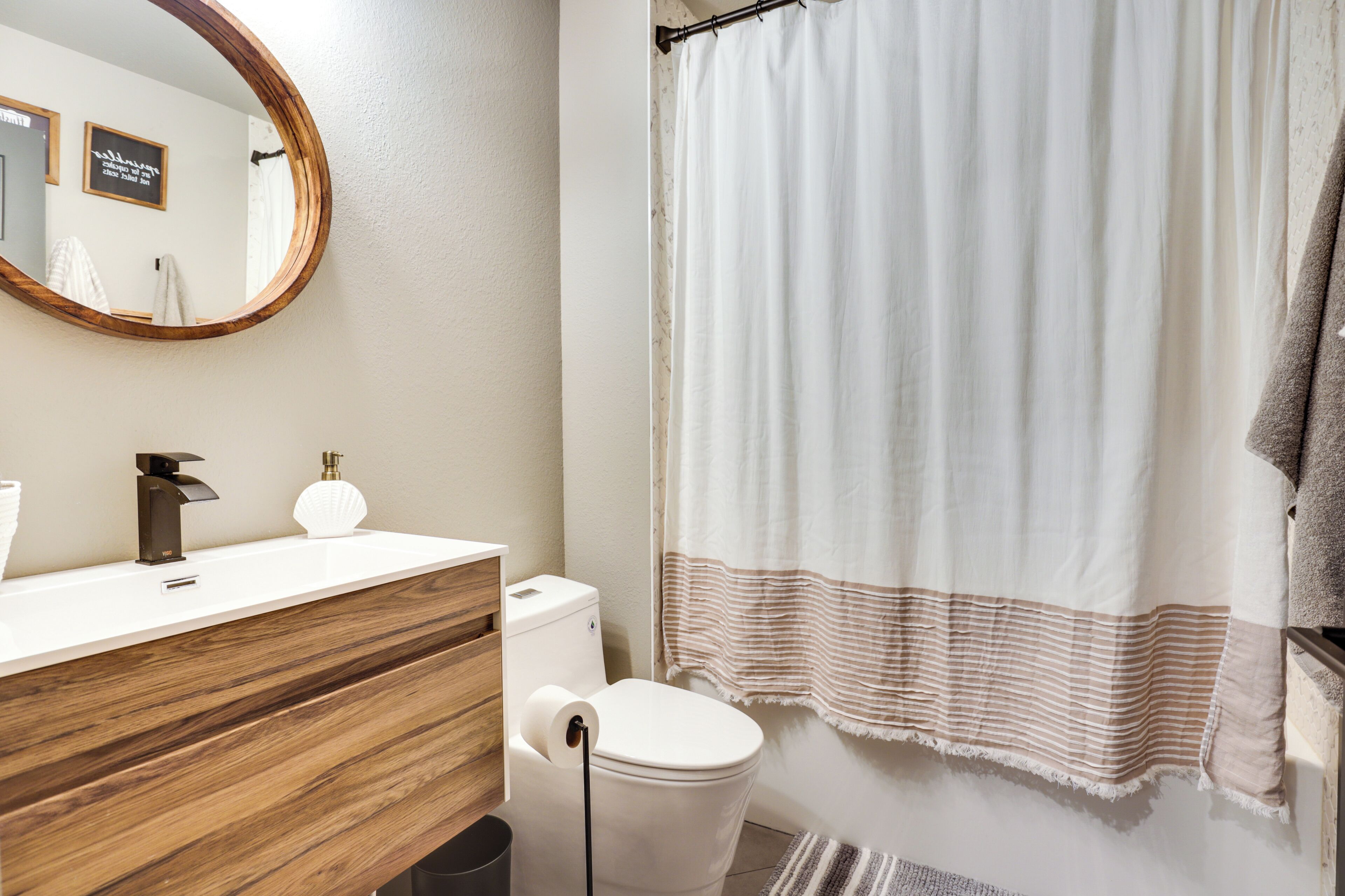 A bathroom with a wooden vanity, a toilet, a shower curtain, and a mirror.
