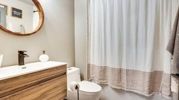 A bathroom with a wooden vanity, a toilet, a shower curtain, and a mirror.
