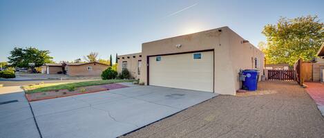A residential garage with a clear driveway, a blue trash bin, and a wooden fence.