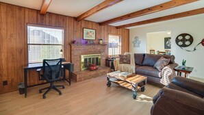 A living room with a fireplace, wooden walls, a sofa, a desk, and a computer chair. - Adobe Home in Albuquerque w/ Covered Patio (Albuquerque)