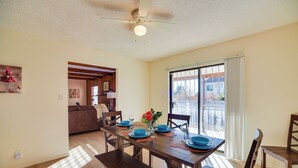 A dining area with a wooden table set for four, a ceiling fan, and a view through a sliding glass door to the outside. - Adobe Home in Albuquerque w/ Covered Patio (Albuquerque)