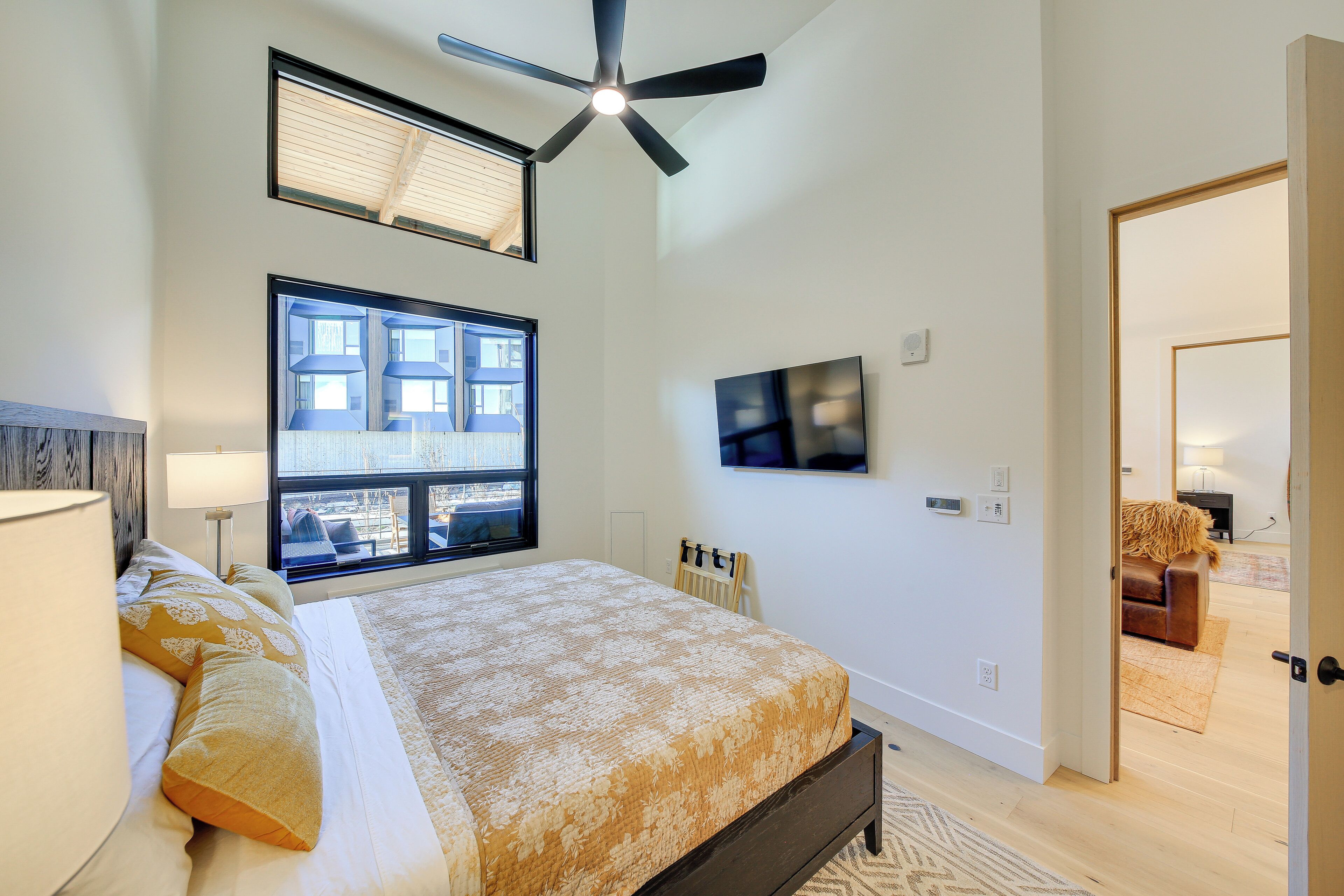 A bedroom with a bed, a ceiling fan, a TV, and a window with blinds.