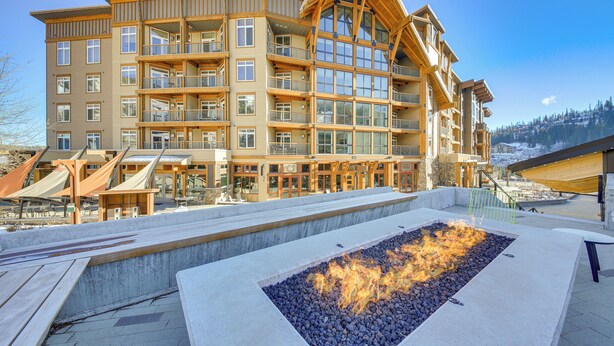 A multi-story hotel with balconies, a fire feature, and a ski slope in the background. - Luxe Schweitzer Condo w/ Hot Tub: Ski-in/ski-out! (Sandpoint)