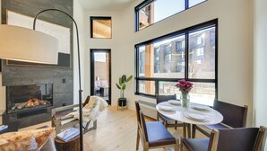 A modern dining area with a fireplace, large windows, and a view of the city. - Luxe Schweitzer Condo w/ Hot Tub: Ski-in/ski-out! (Sandpoint)
