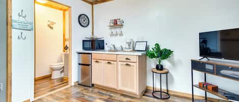 A compact kitchen with wooden flooring, a built-in microwave, a coffee maker, and a TV on a stand.
