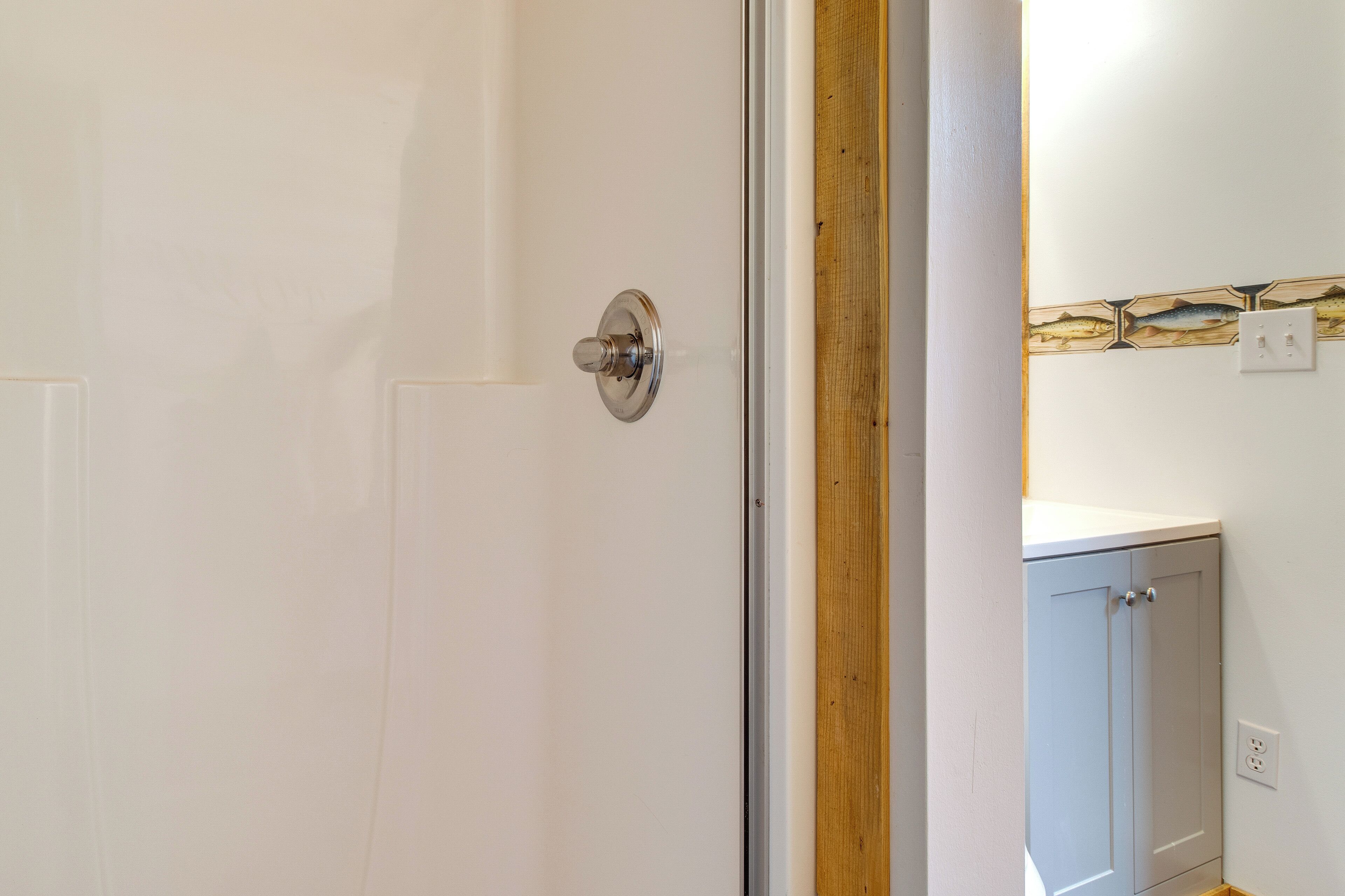 Una puerta blanca con un picaporte plateado, un marco de madera y un rebozado de azulejos con motivos de peces.