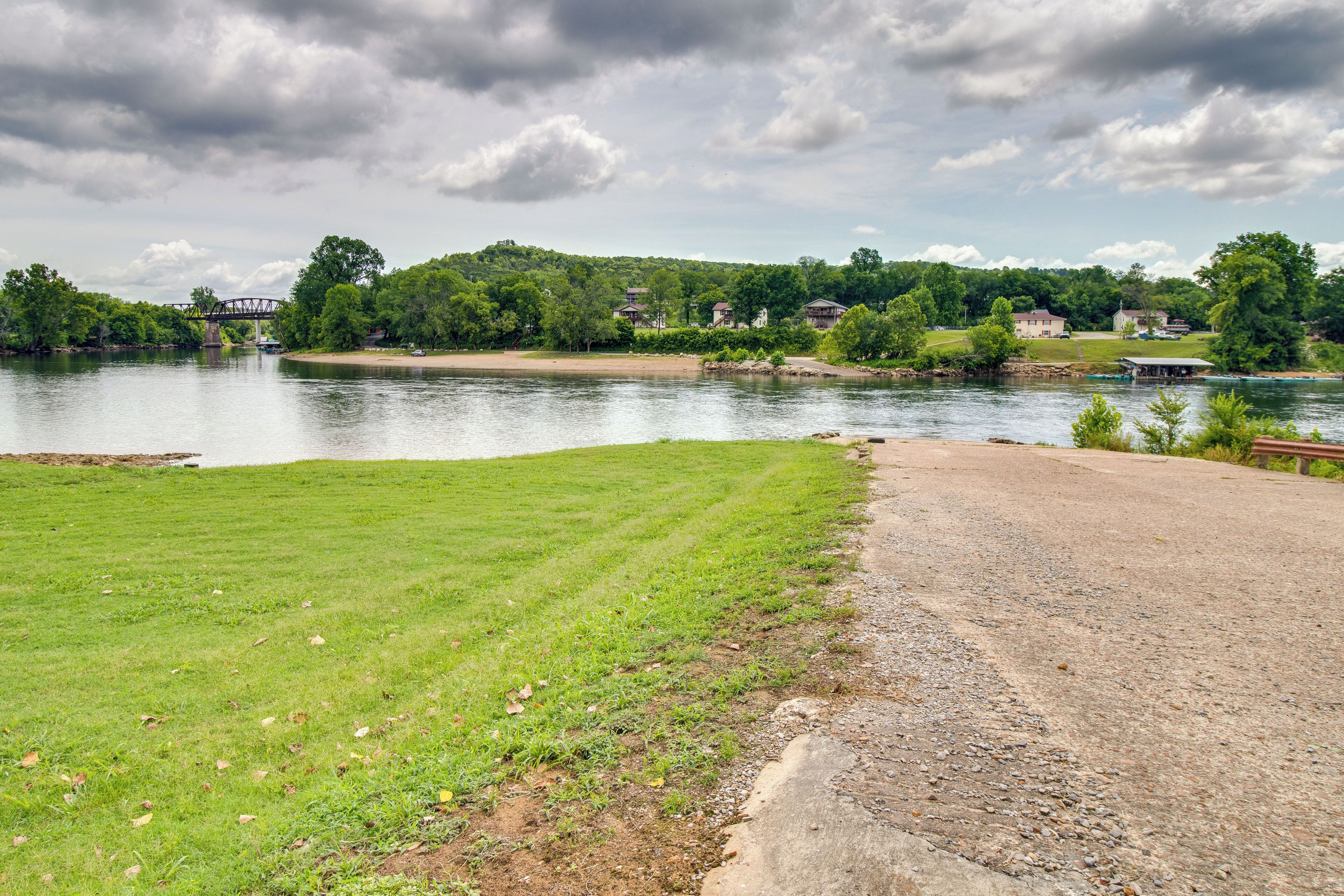 A riverside view with a grassy area, a concrete path, and a bridge in the distance.