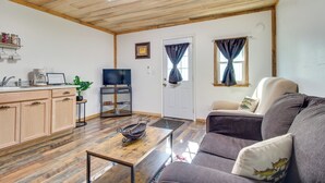 Ein Wohnzimmer mit Holzboden, einer Couch, einem Couchtisch, einem Fernseher und einer Küchenzeile mit Schränken und einer Kaffeemaschine.
