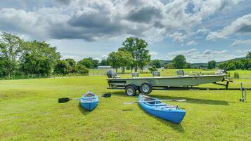 A grassy field with two kayaks and a boat trailer.
