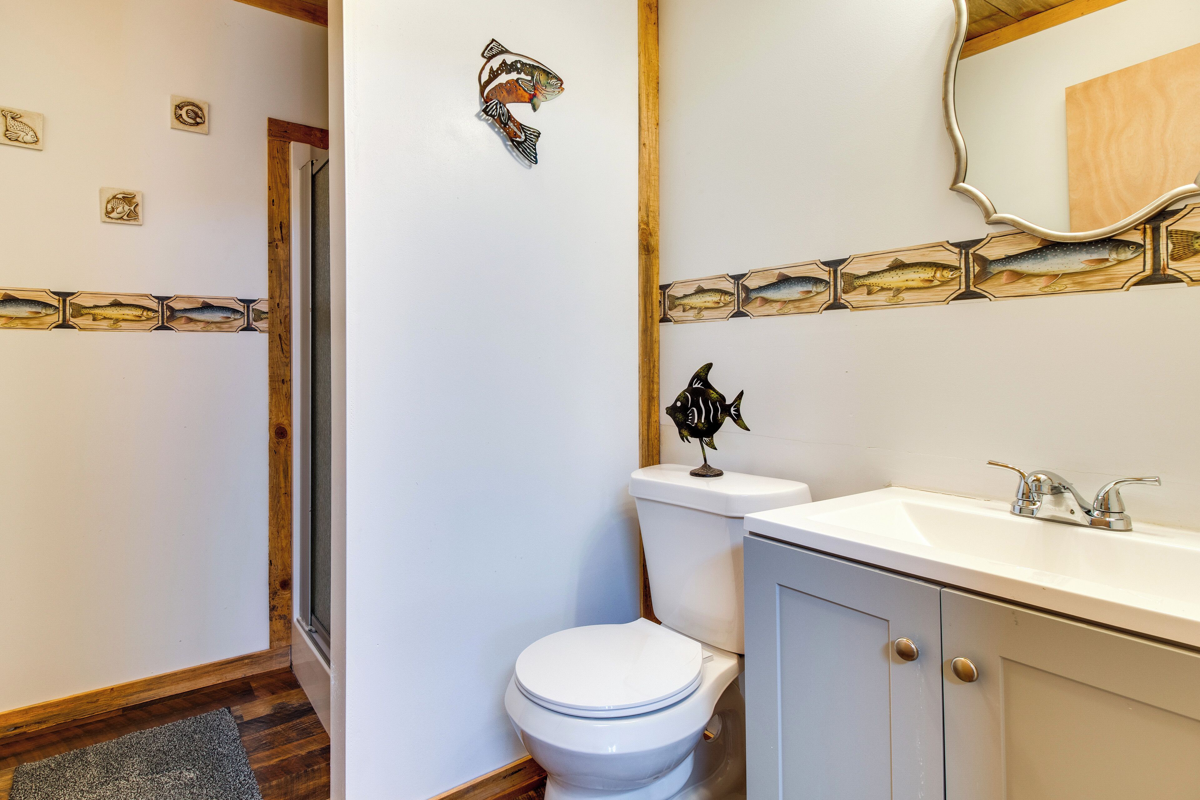 Une salle de bain avec des toilettes blanches, un lavabo avec un miroir et des décorations murales représentant des poissons.