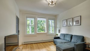 Un salon avec un canapé d’angle gris, une petite table d’appoint sur laquelle est posée une plante, et trois tableaux encadrés accrochés au mur.
