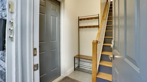 Un couloir avec une porte grise, un présentoir en métal et un escalier en bois.