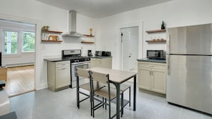 Une cuisine moderne avec des meubles blancs, un réfrigérateur en acier inoxydable, une table à manger en bois et une cuisinière encastrée.