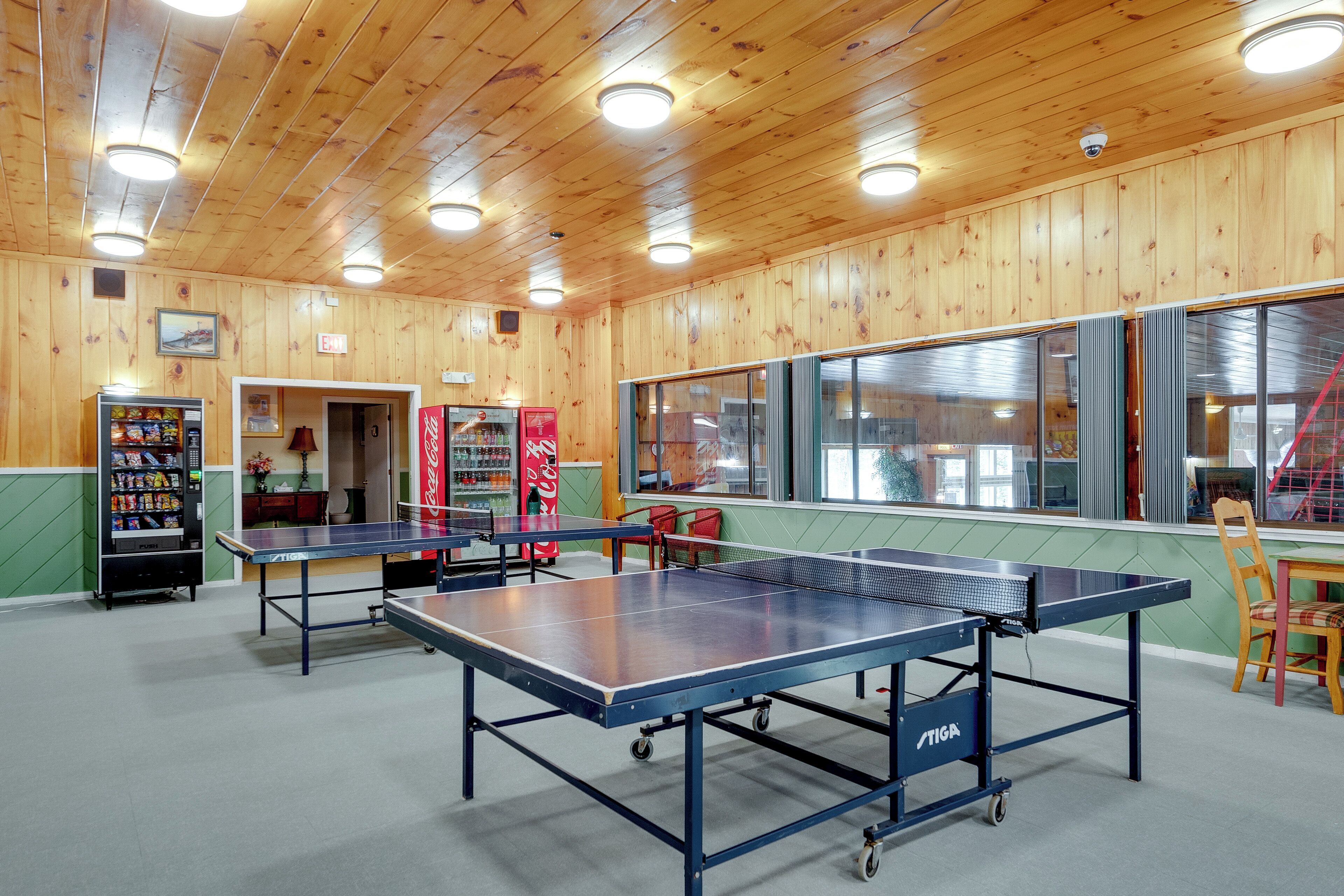 A room with wooden walls, a ping pong table, a Coca-Cola refrigerator, and a vending machine.