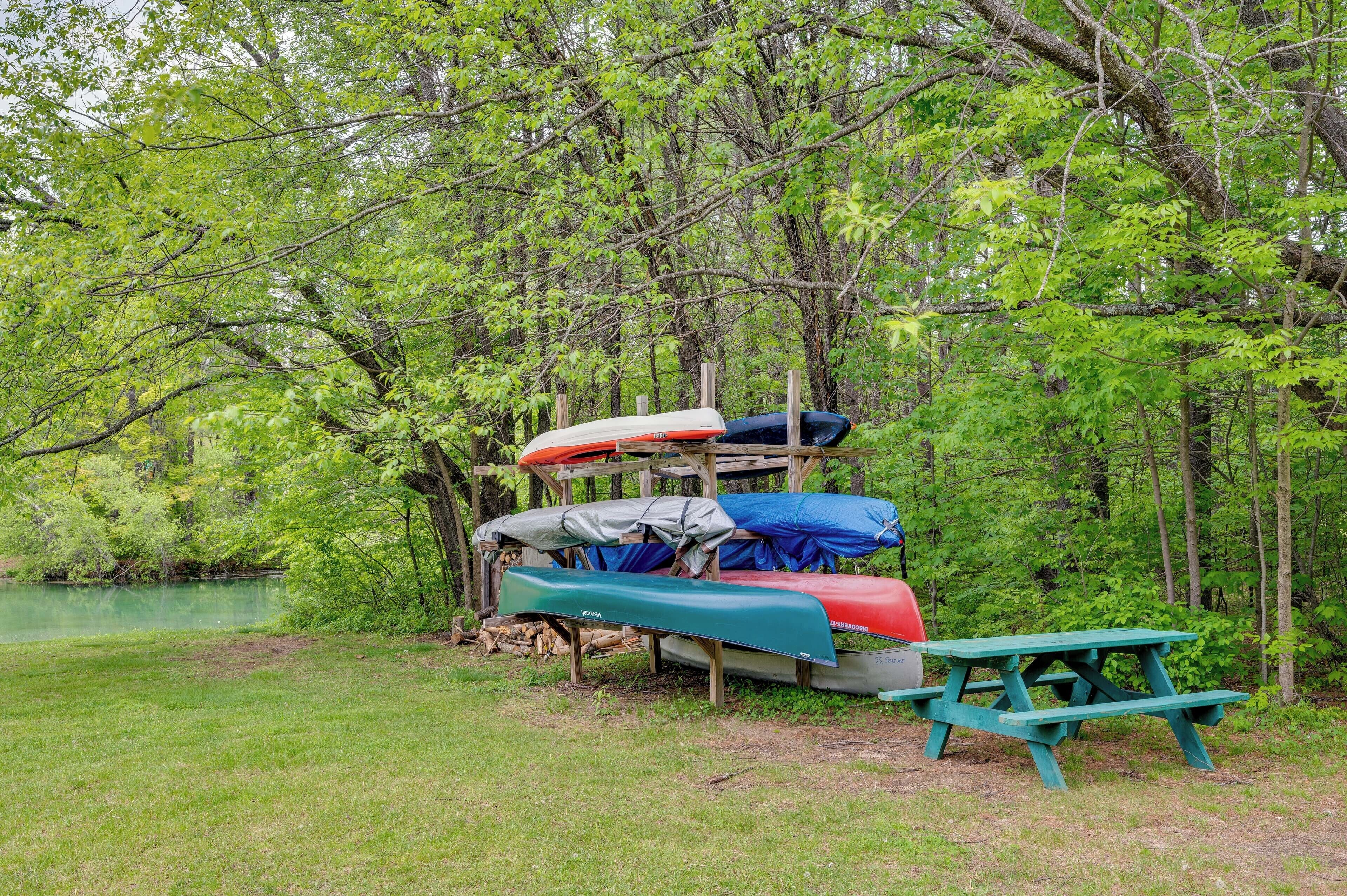 A row of canoes and a picnic table in a wooded area.