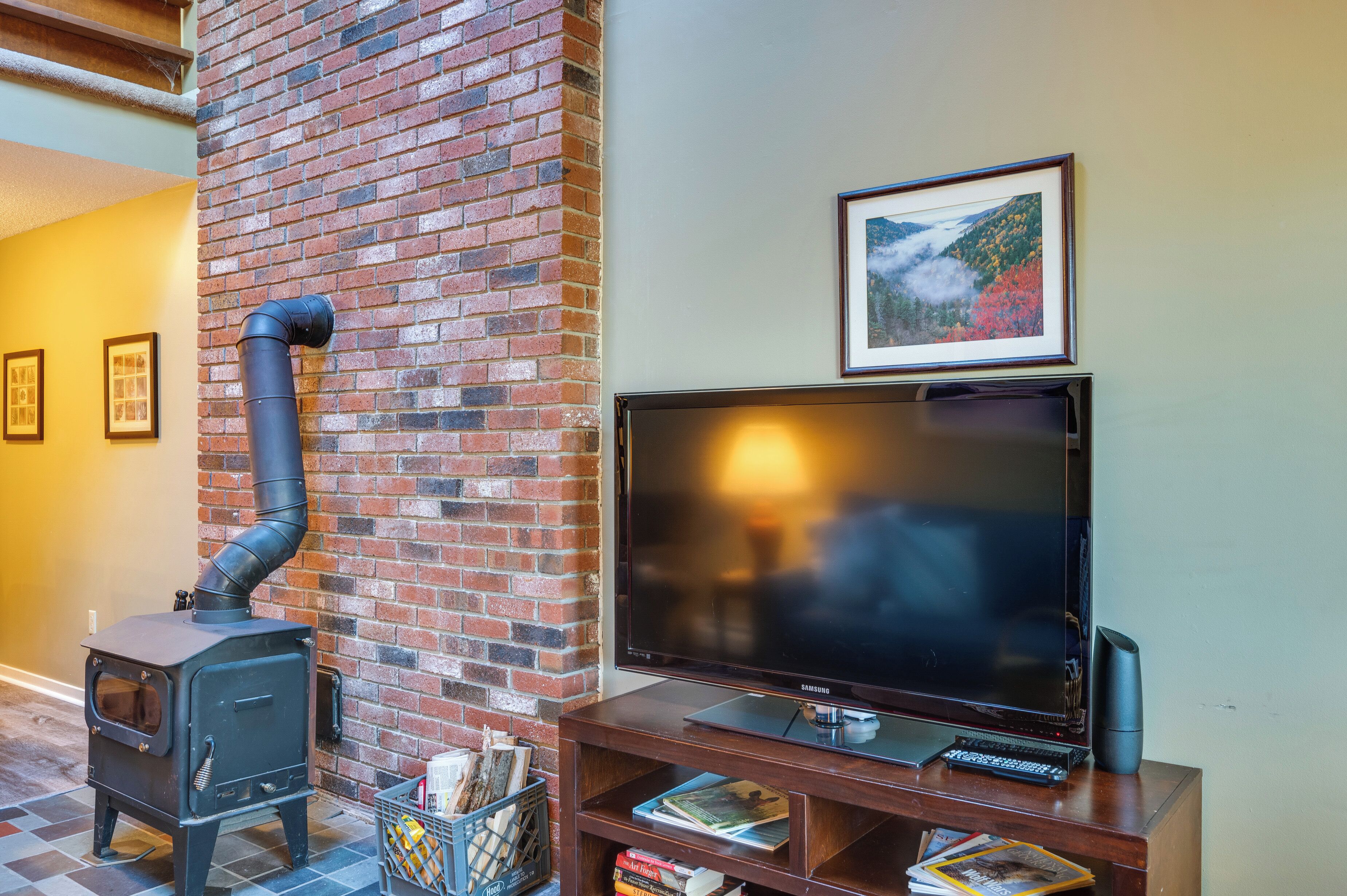 A living room with a brick fireplace, a flat-screen TV, and a framed picture on the wall.